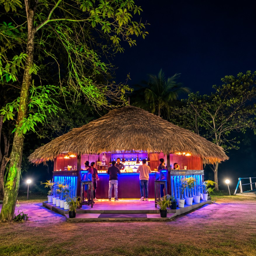Thatched-roof outdoor bar with colourful lighting and guests at Digaru Eco Resort in Arunachal Pradesh.